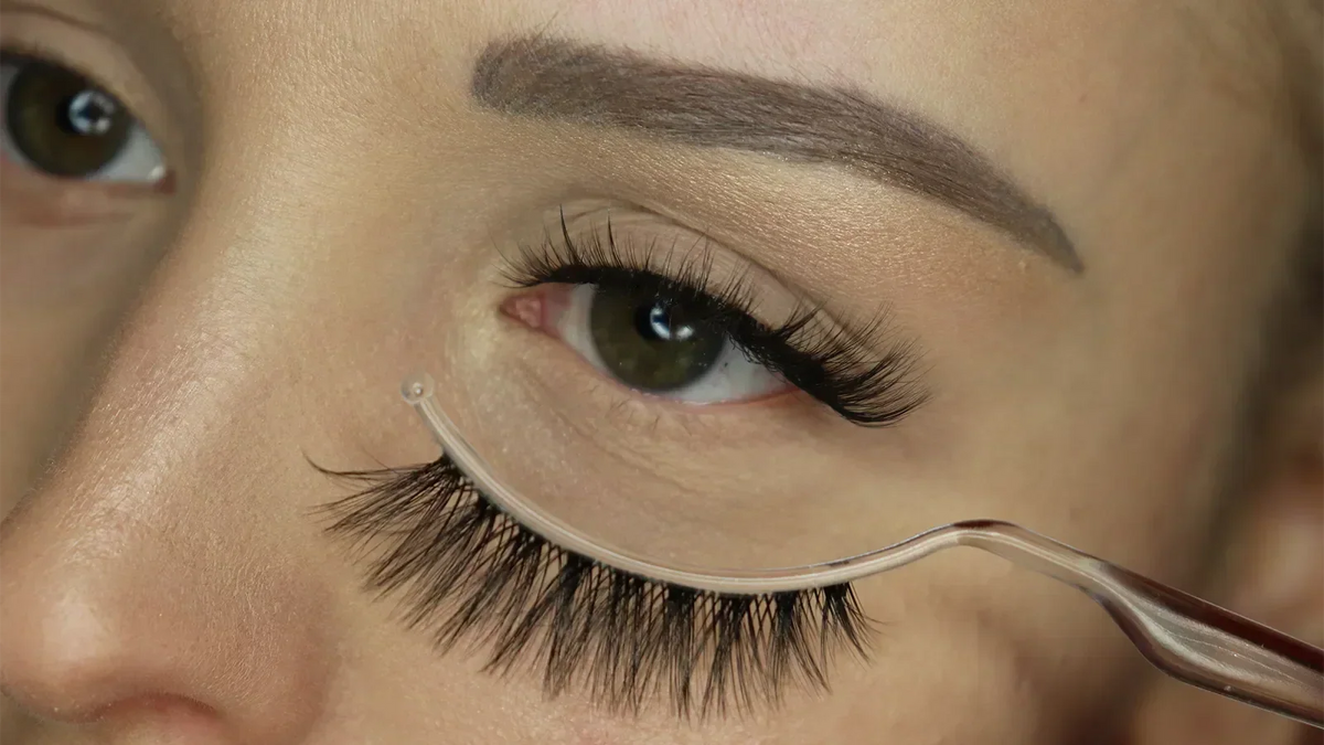 Nahaufnahme eines Auges mit aufgeklebten Fox-Eye-Wimpern von MARIOR, darunter wird eine zweite falsche Wimper mit einem Applikator an das Auge gehalten